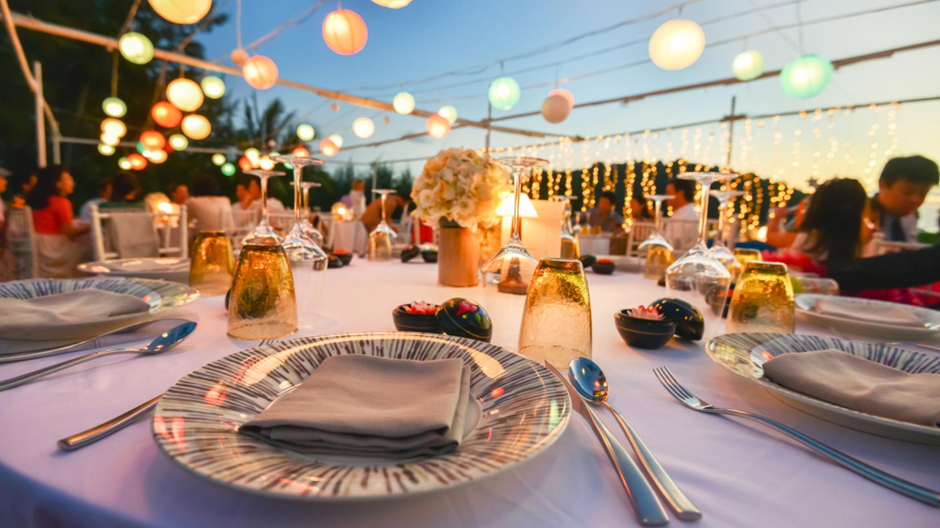 Cena all'aperto con luci colorate e tavola elegantemente apparecchiata.