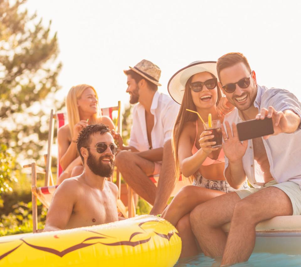Amici si divertono in piscina, scattano selfie e bevono drink al sole.